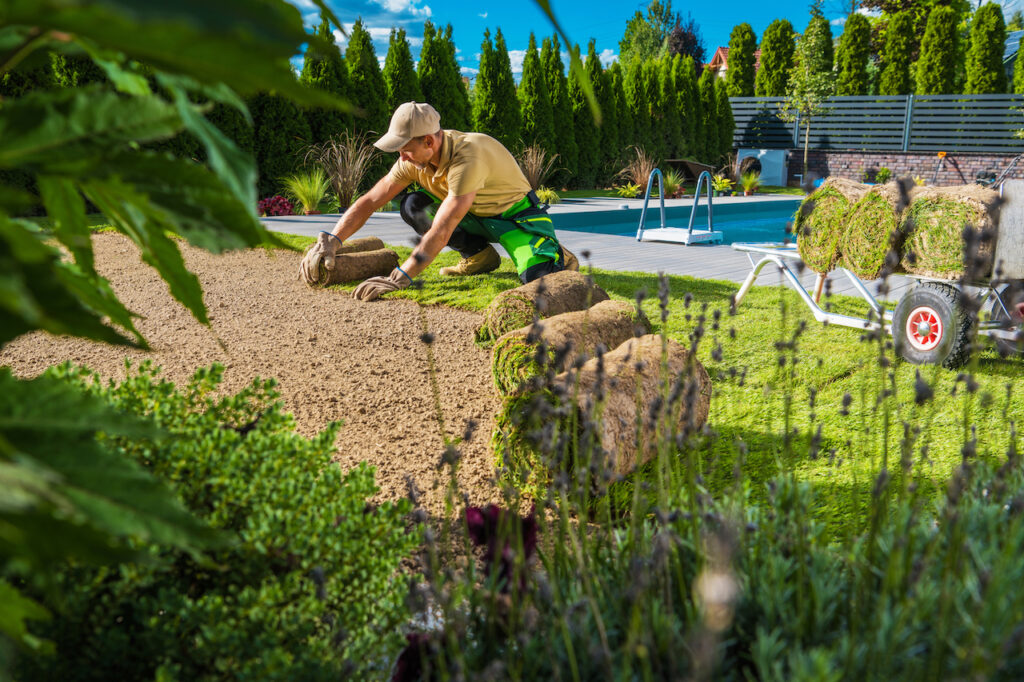 man laying sod by swimming pool at new home build